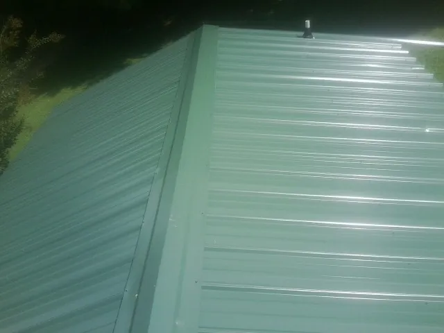 New green metal panels meeting at the ridge of a roof — Flat Roof Repair work by our crew in Hickory