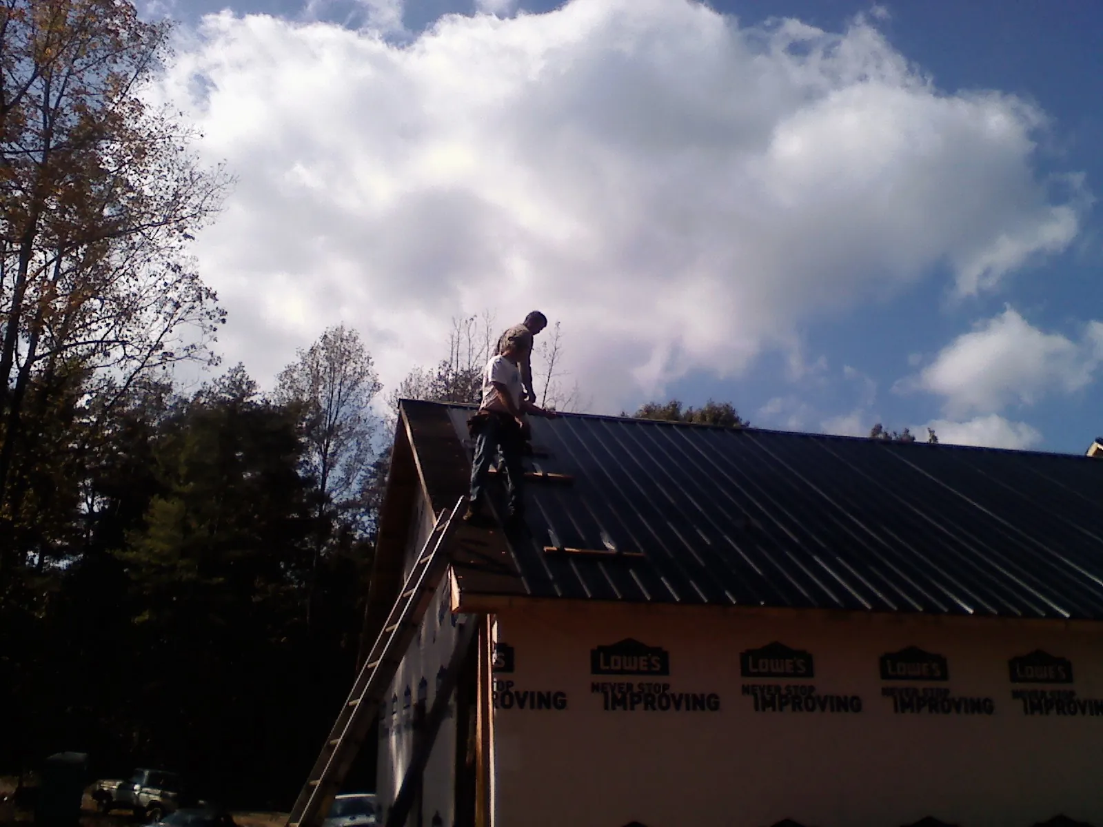 Roofer fastening dark metal panels high against a cloudy sky, from a Roof Inspection job in Hickory