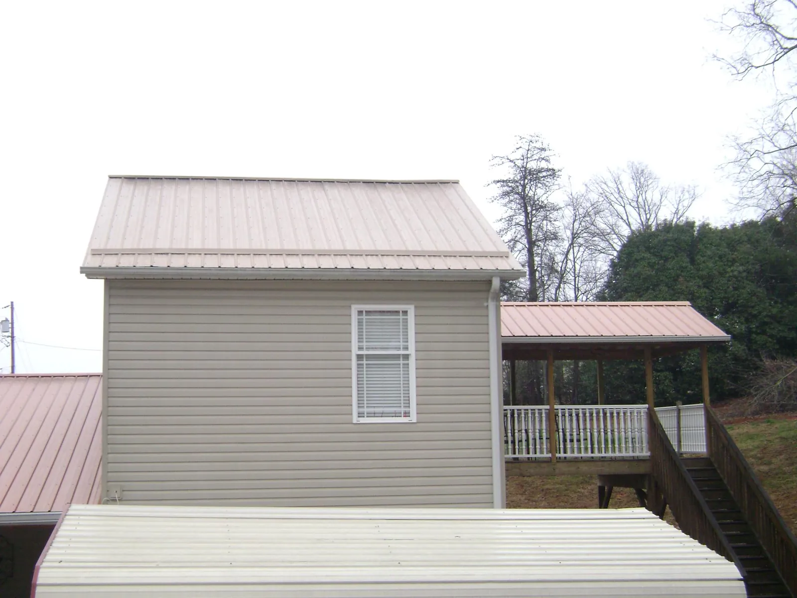 Tan metal roofs on a two story addition and attached porch, from a Roof Replacement job in Hickory